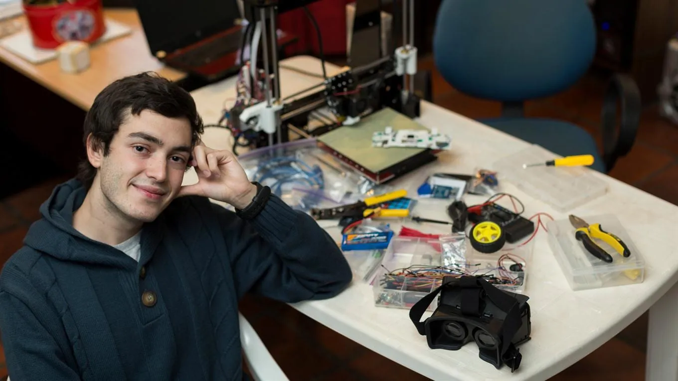 Marcos Bruno in his workshop, next to a 3D printer and robotics components